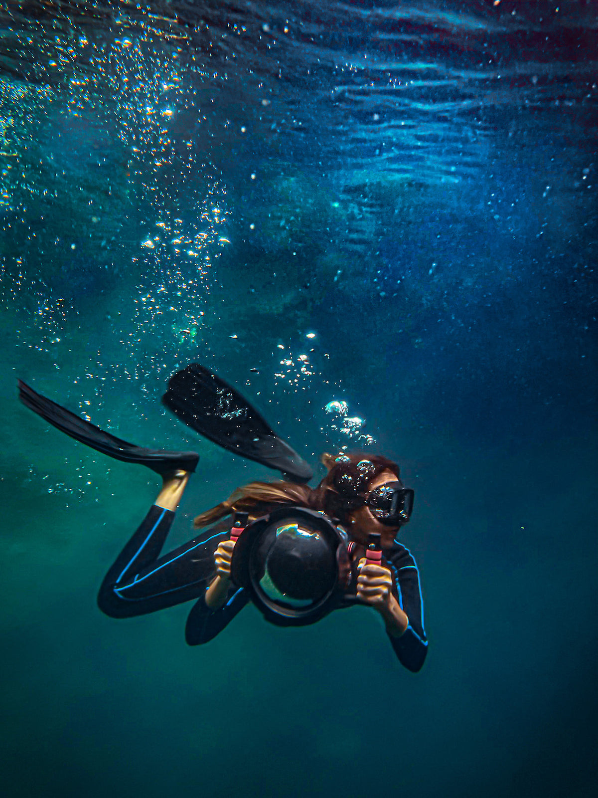 DreamArt underwater photographer in a wetsuit and fins diving with a camera in a cenote