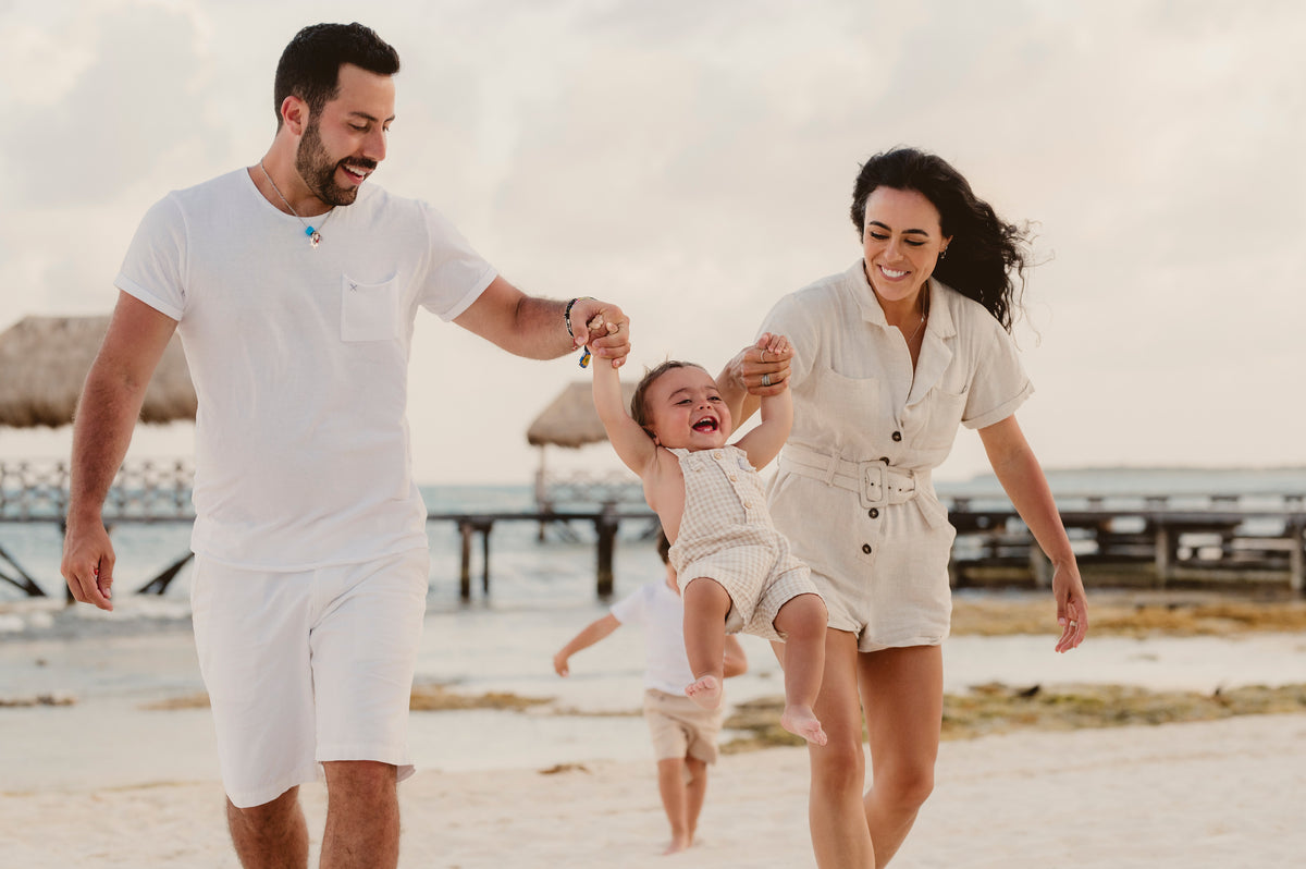 Parents swing their laughing toddler by the hands on the beach during a family photoshoot at Vidanta