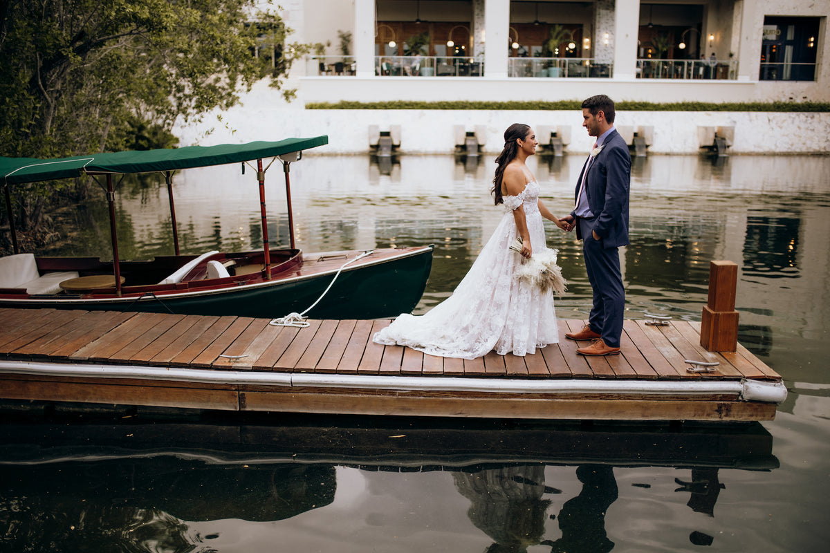 A bride and groom hold hands on a wooden dock beside a docked boat at the resort
