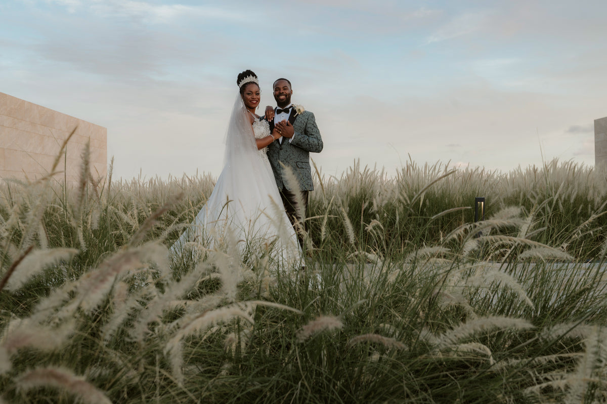 Bride and groom stand among wild grasses at dusk during their destination wedding photoshoot