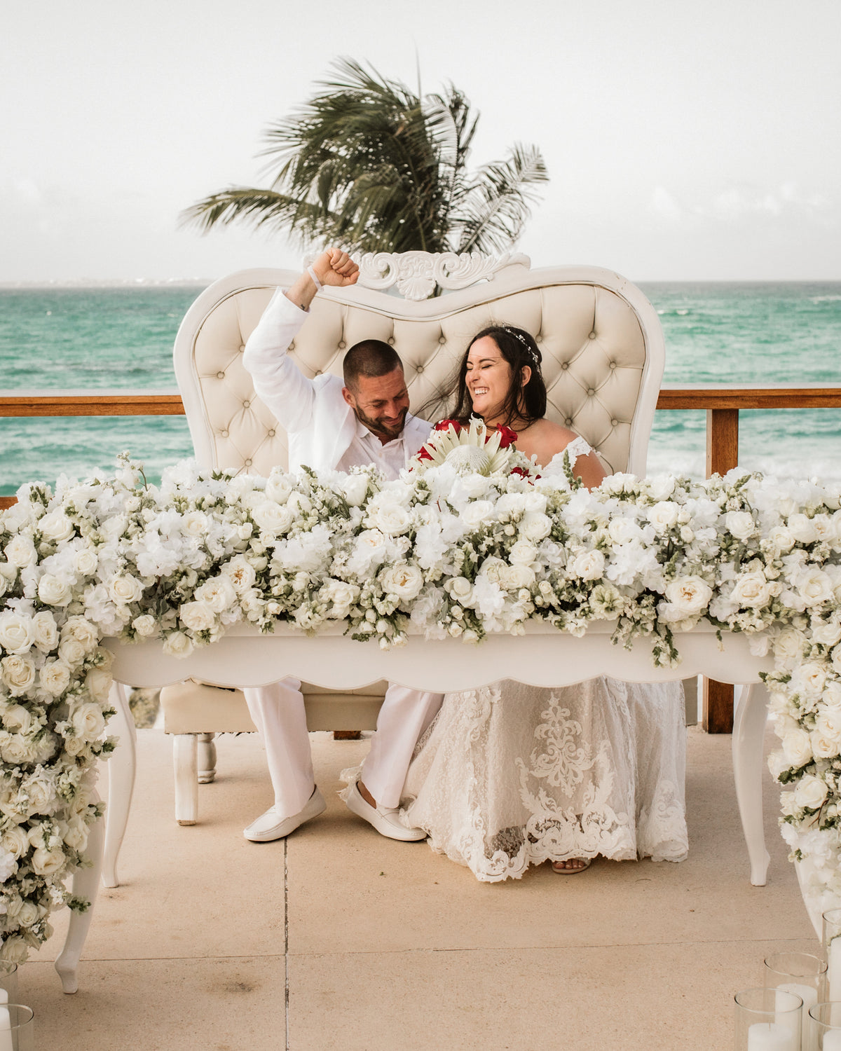 A bride and groom laugh together at a flower-covered table overlooking the ocean at Grand Fiesta Americana Coral Beach Cancún