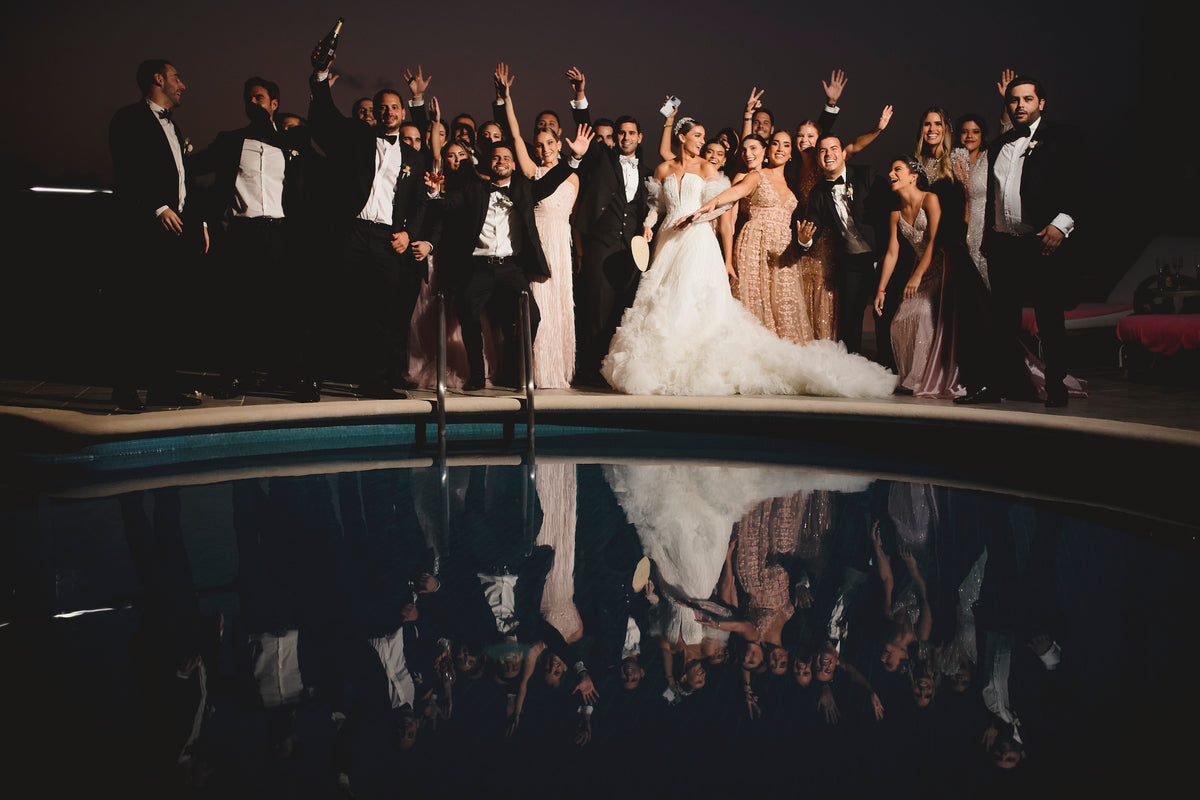 Wedding party celebrates poolside at night at Grand Fiesta Americana Coral Beach Cancún, reflection visible in water