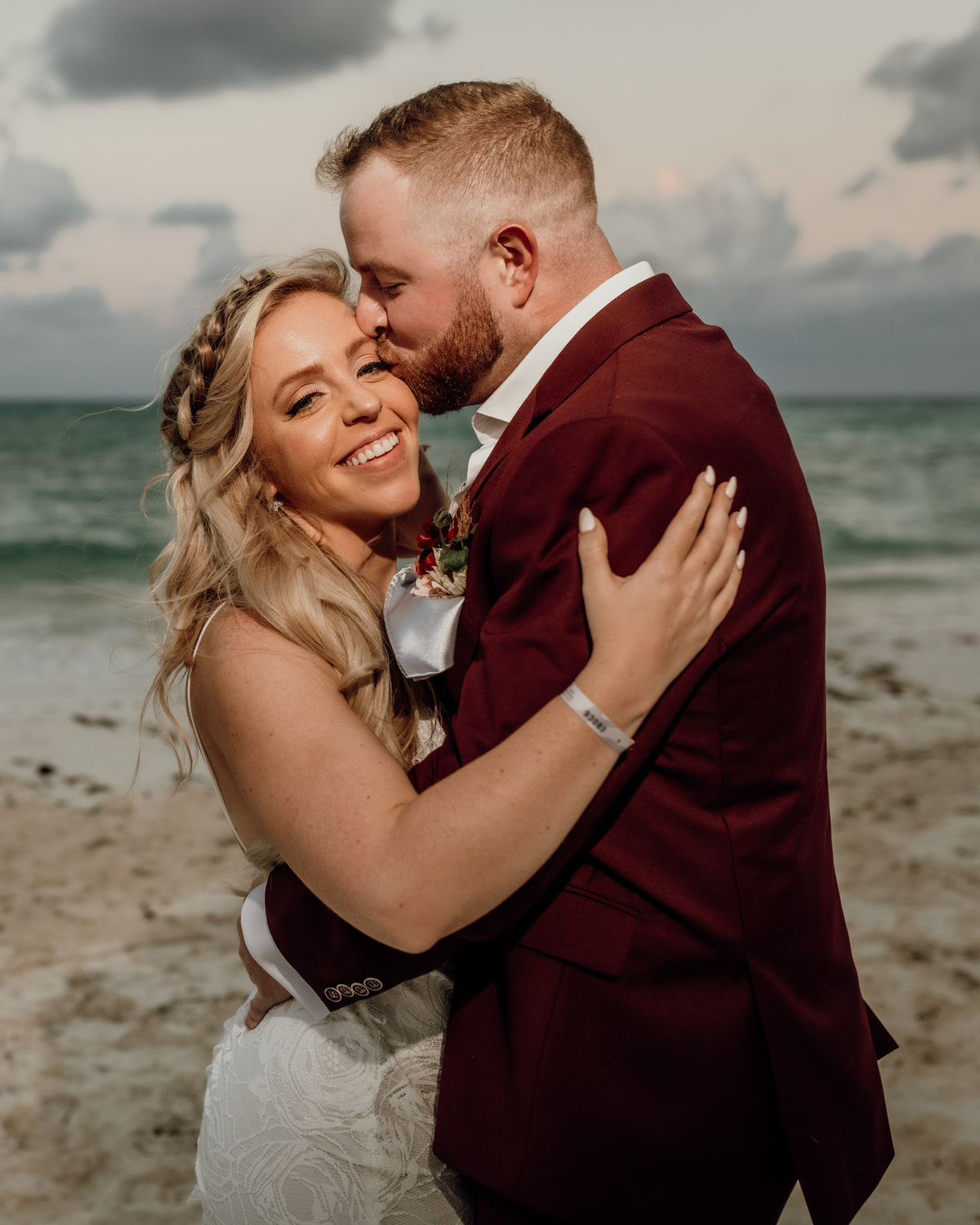 Bride and groom embrace on the beach at Grand Fiesta Americana Coral Beach Cancún, groom kissing her forehead