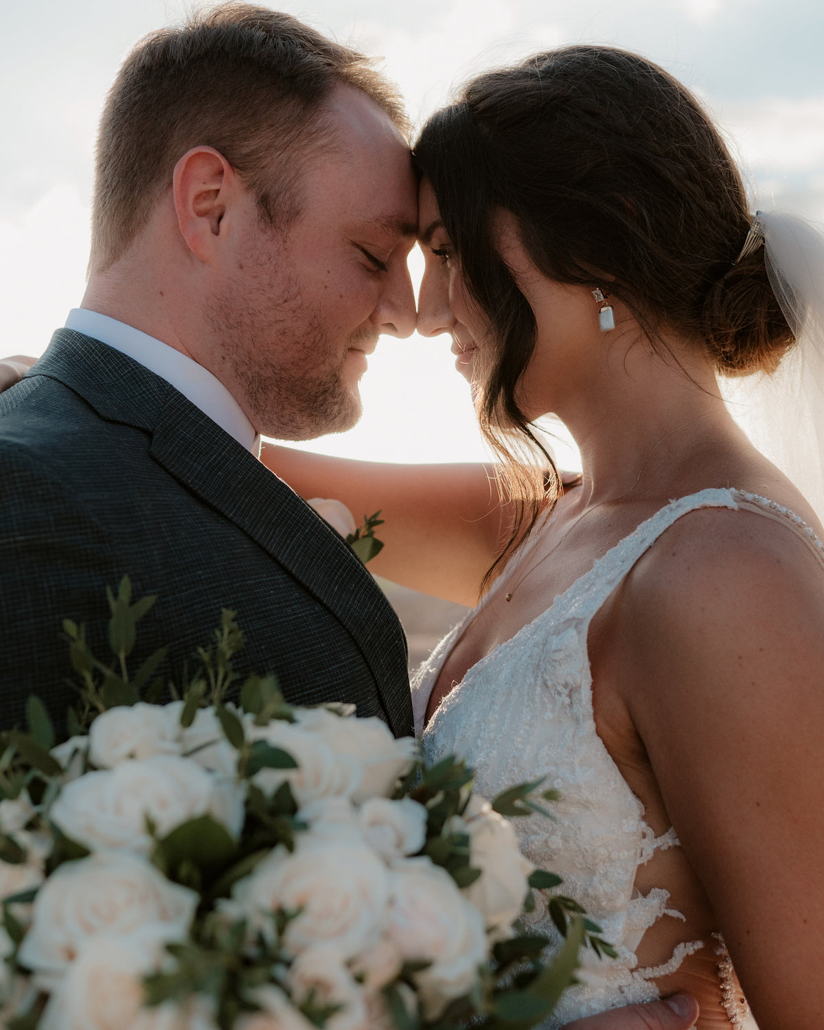 Bride and groom touch foreheads smiling, holding a white rose bouquet at Fiesta Americana Los Cabos