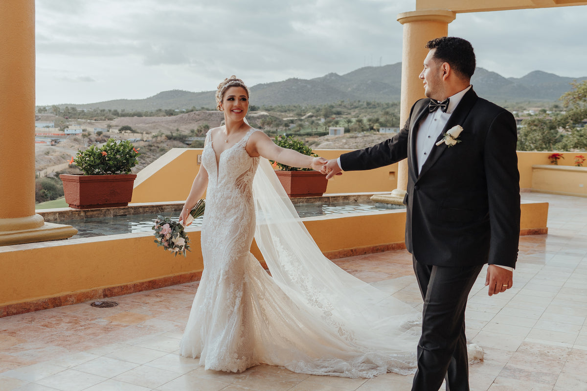 A bride and groom hold hands on a terrace at Fiesta Americana Los Cabos with mountains behind them