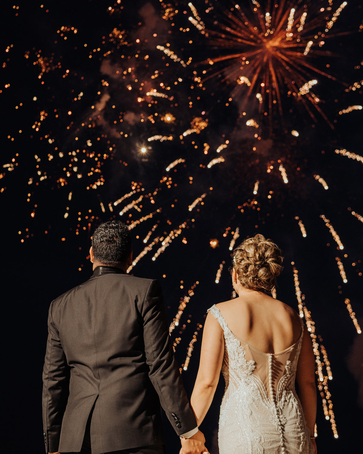 A bride and groom hold hands watching fireworks light up the night sky at Fiesta Americana Los Cabos
