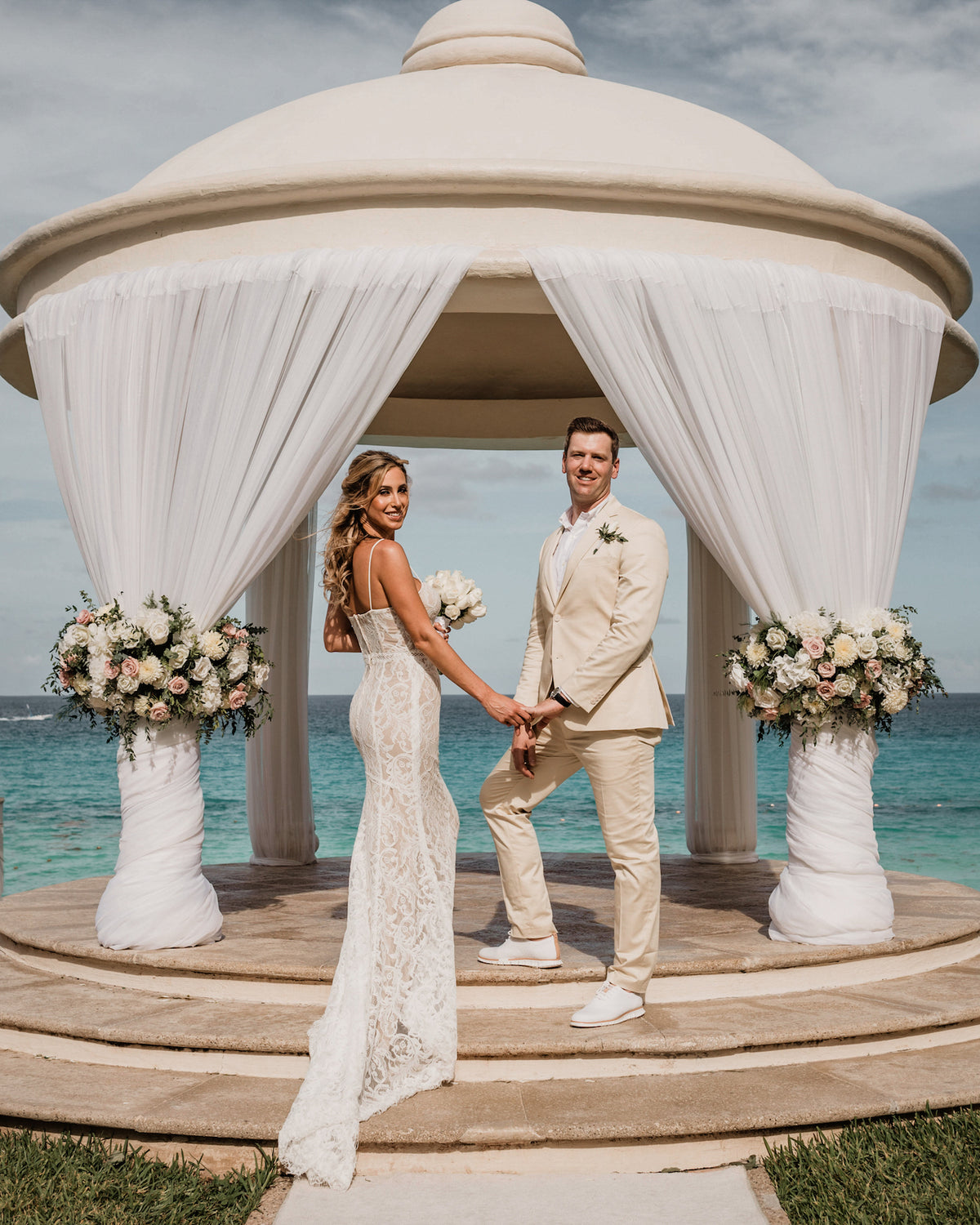 Bride and groom hold hands beneath a domed gazebo overlooking the ocean at JW Marriott