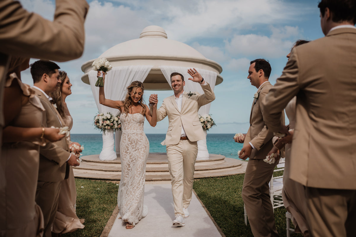 Bride and groom raise joined hands walking down the aisle at their JW Marriott beach wedding