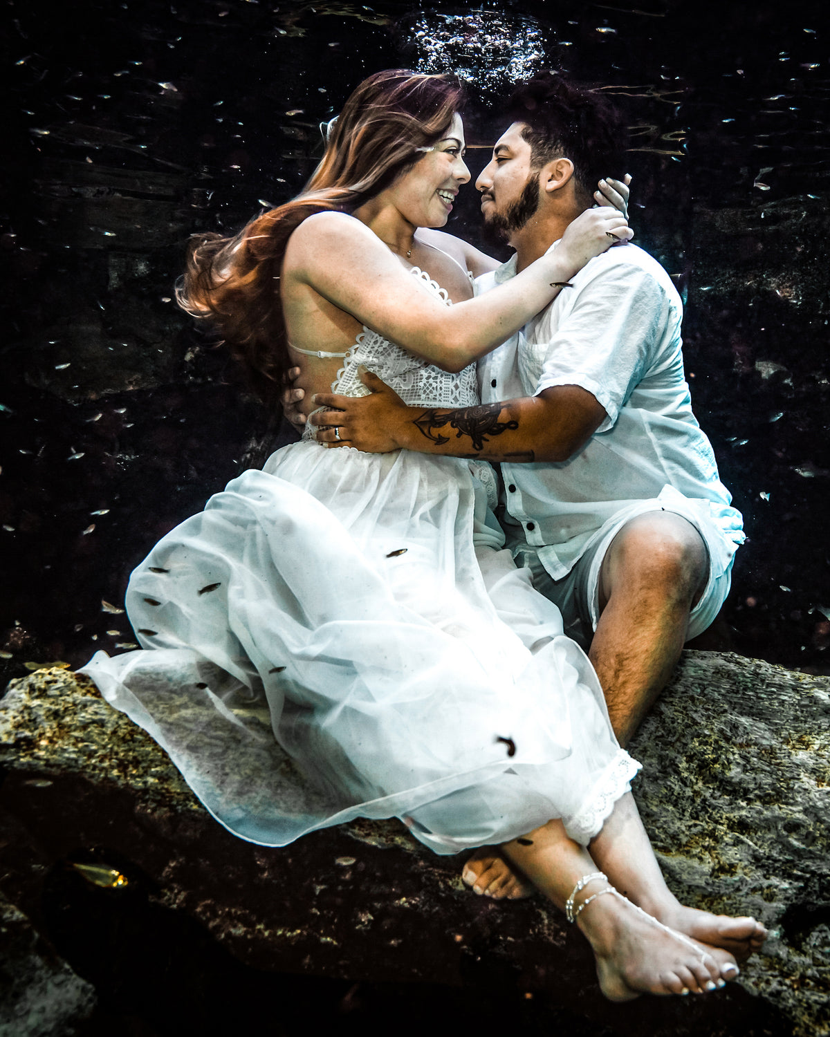 A couple embraces underwater in a cenote-style pool near Moon Palace Cancún, small fish swimming around them