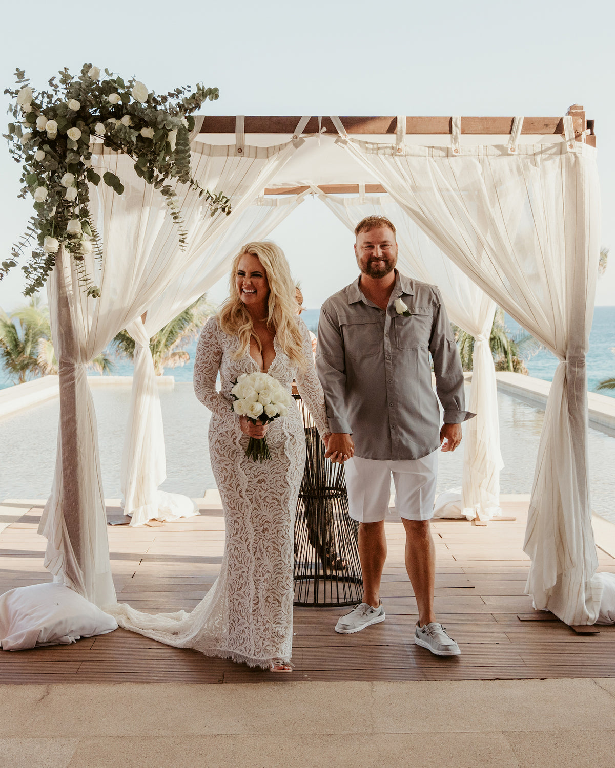 Bride and groom hold hands under a draped canopy at Marquis Los Cabos, ocean and pool behind them