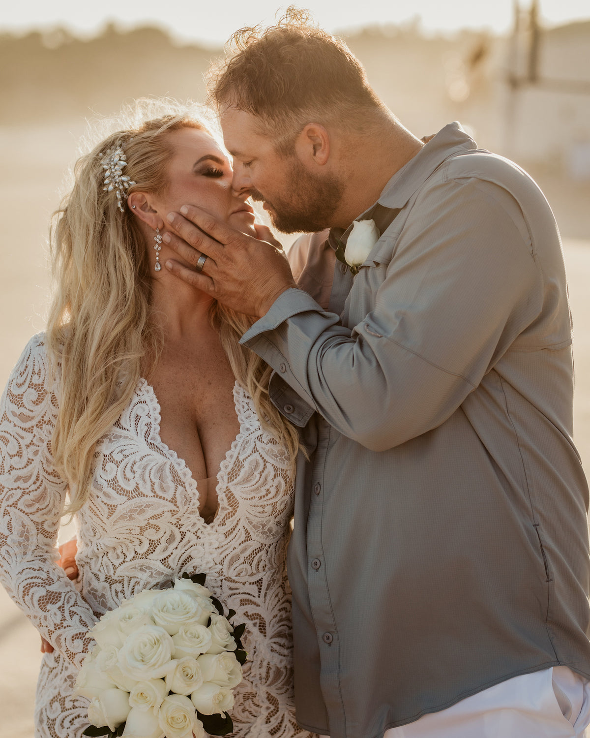 Bride and groom close together outdoors at Marquis Los Cabos, he cups her face, she holds a white rose bouquet