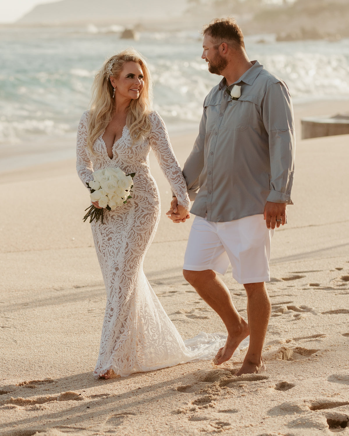 Bride and groom hold hands walking barefoot on the beach at Marquis Los Cabos with waves behind them