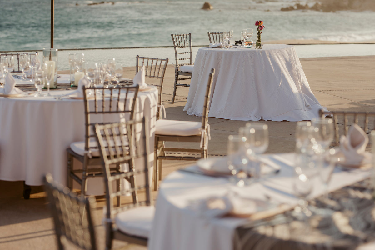 Round tables with white linens and chiavari chairs set for a reception overlooking the ocean at Marquis Los Cabos
