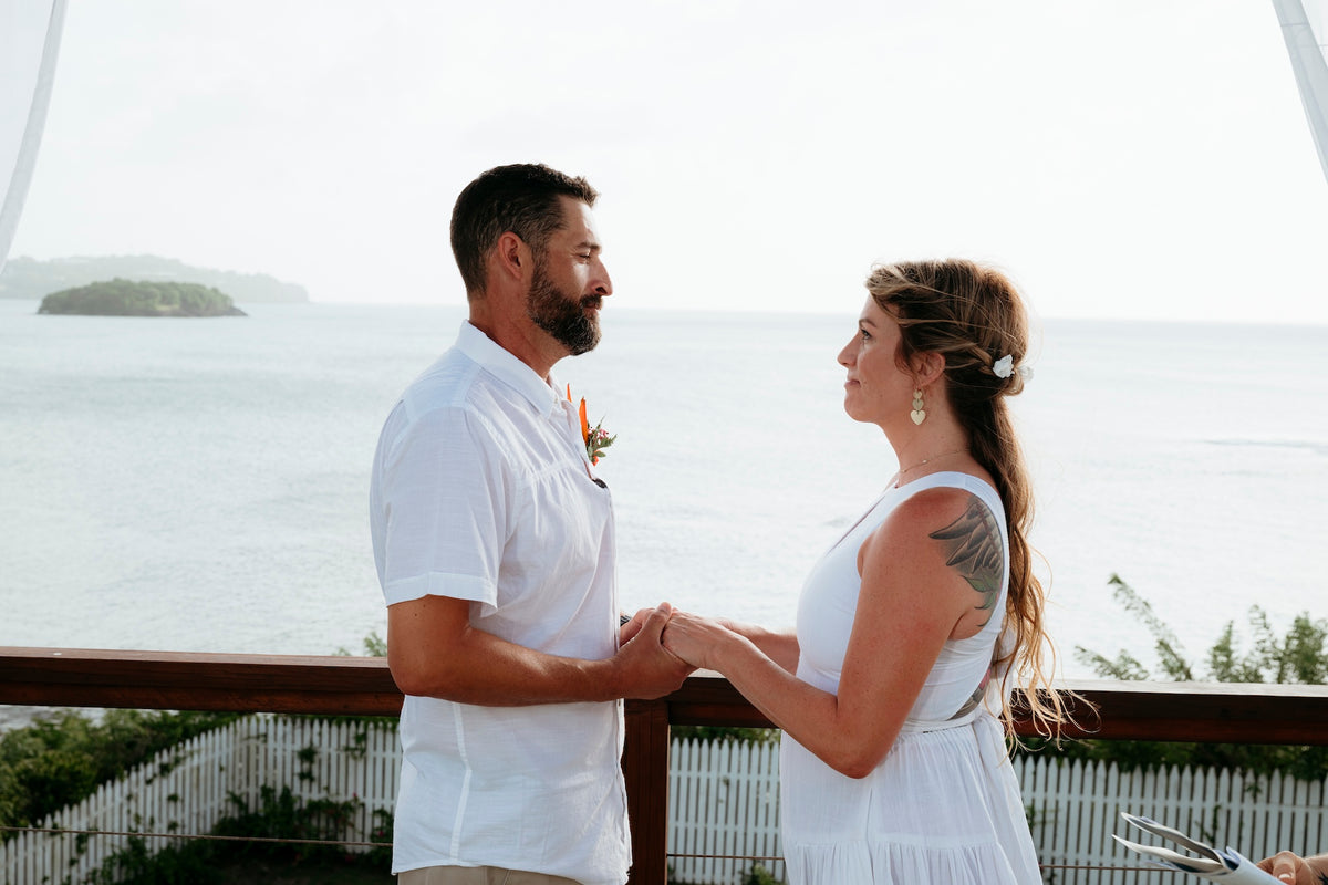 A couple holds hands during a seaside wedding ceremony overlooking the ocean and small island