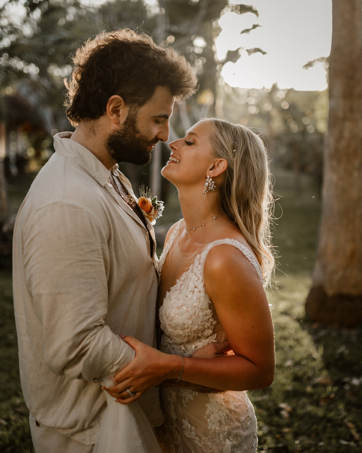 Bride and groom embrace face to face at Valentin Imperial Riviera Maya, backlit by golden sunlight among trees