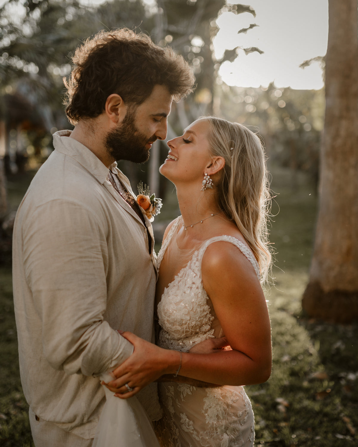 A bride and groom embrace face to face at Valentin Imperial Riviera Maya, backlit by sunlight among trees