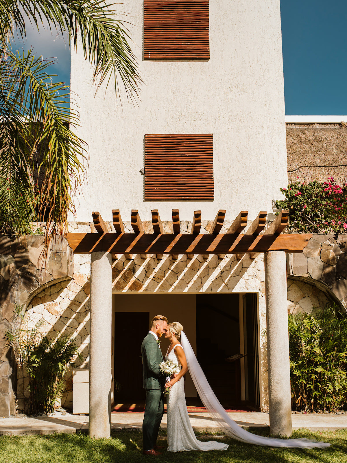 Bride and groom embrace beneath a stone pergola entrance at Valentin Imperial Riviera Maya