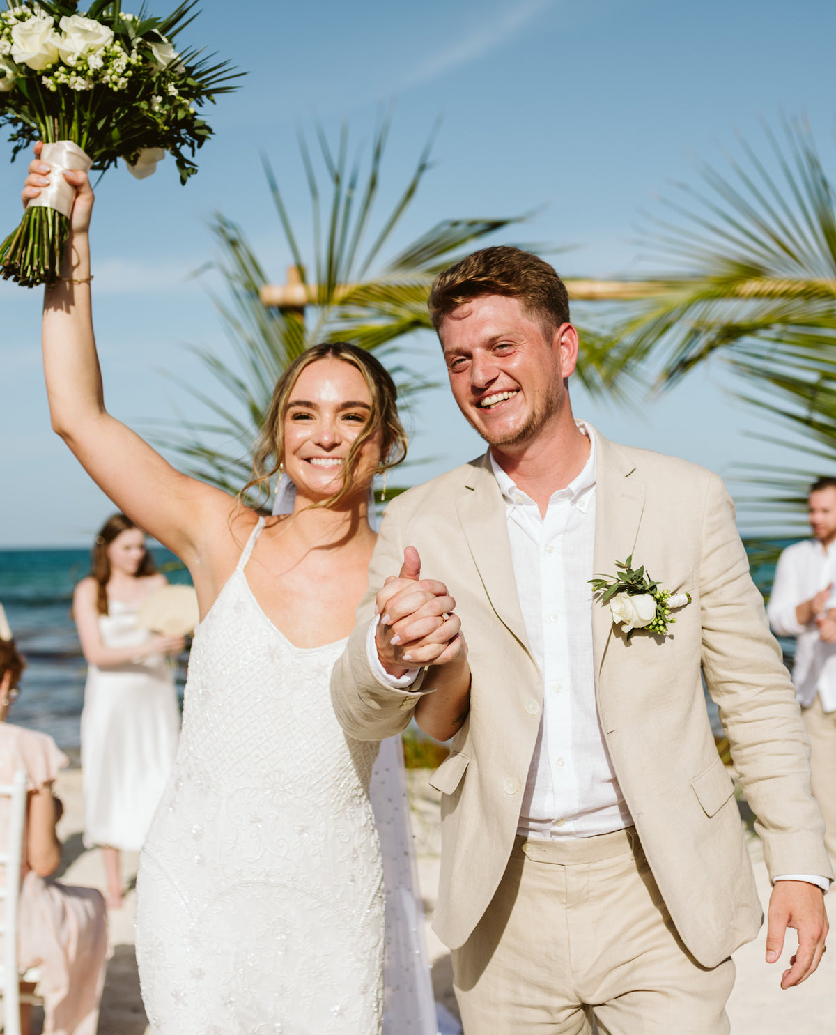 Bride and groom raise clasped hands on the beach at Valentin Imperial Riviera Maya, Mexico
