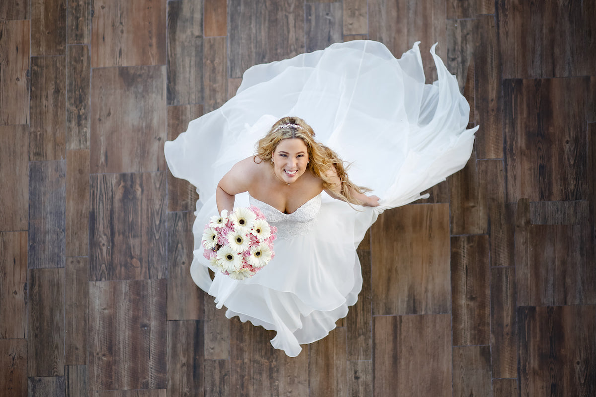 Overhead shot of a smiling bride with her flowing gown spread across a wooden floor at Azul Fives