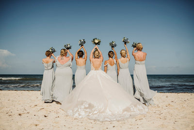 Bride and bridesmaids raise their bouquets on the beach