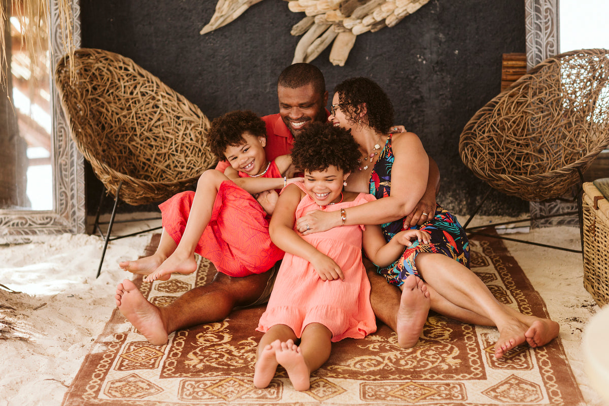 Family of four cuddle and laugh on a patterned rug in a boho beach lounge in Cancun