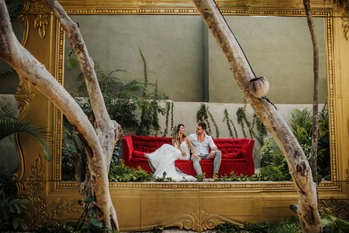 Couple seated on a red velvet sofa inside a gilded frame installation at Casa Malca Tulum