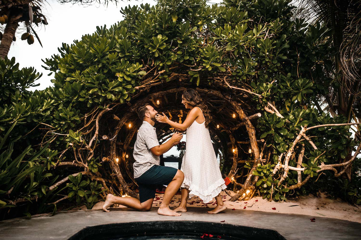 Man kneels to propose to his partner under a lit wooden arch in the jungle at Casa Malca