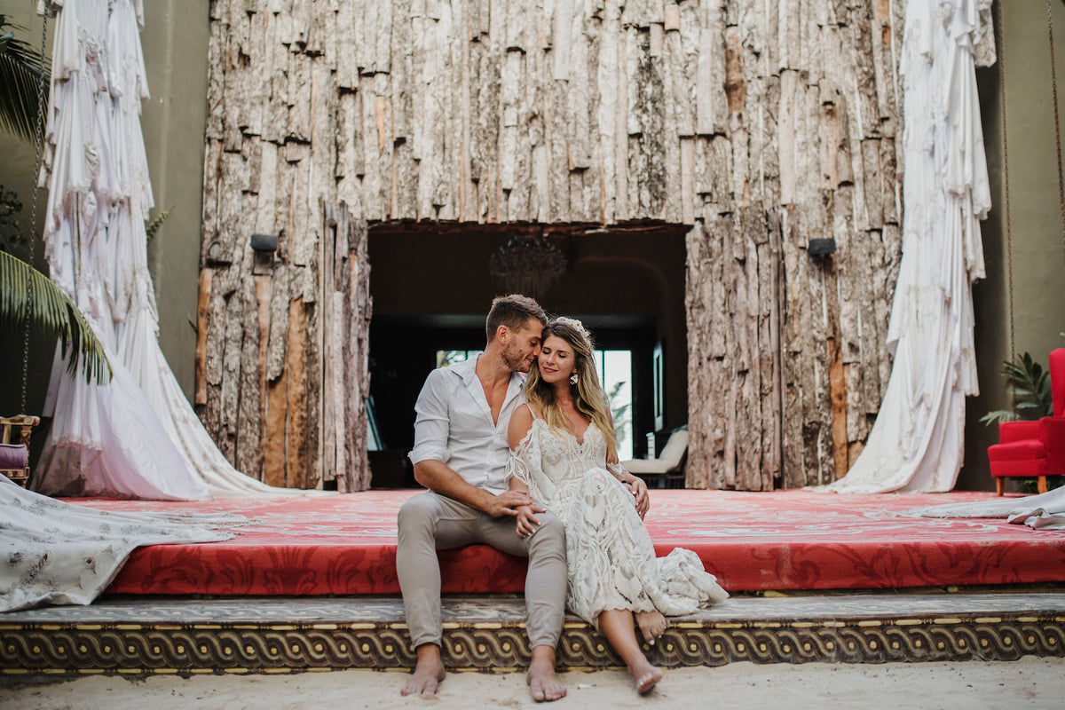 Newlyweds sit barefoot on a red stage before a rustic timber wall at Casa Malca in Tulum