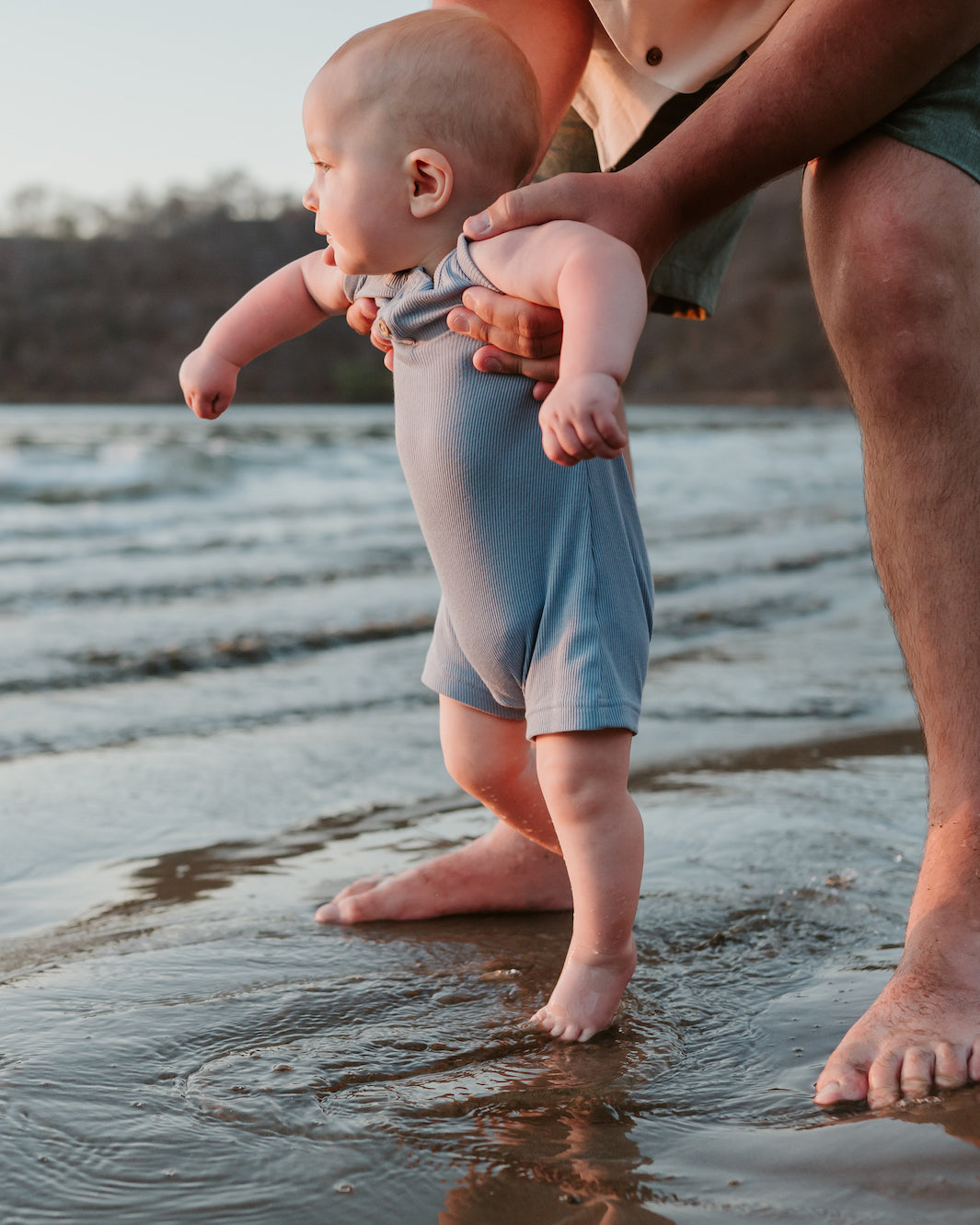 Parent holds a baby taking first steps in shallow water during a Costa Rica family photoshoot
