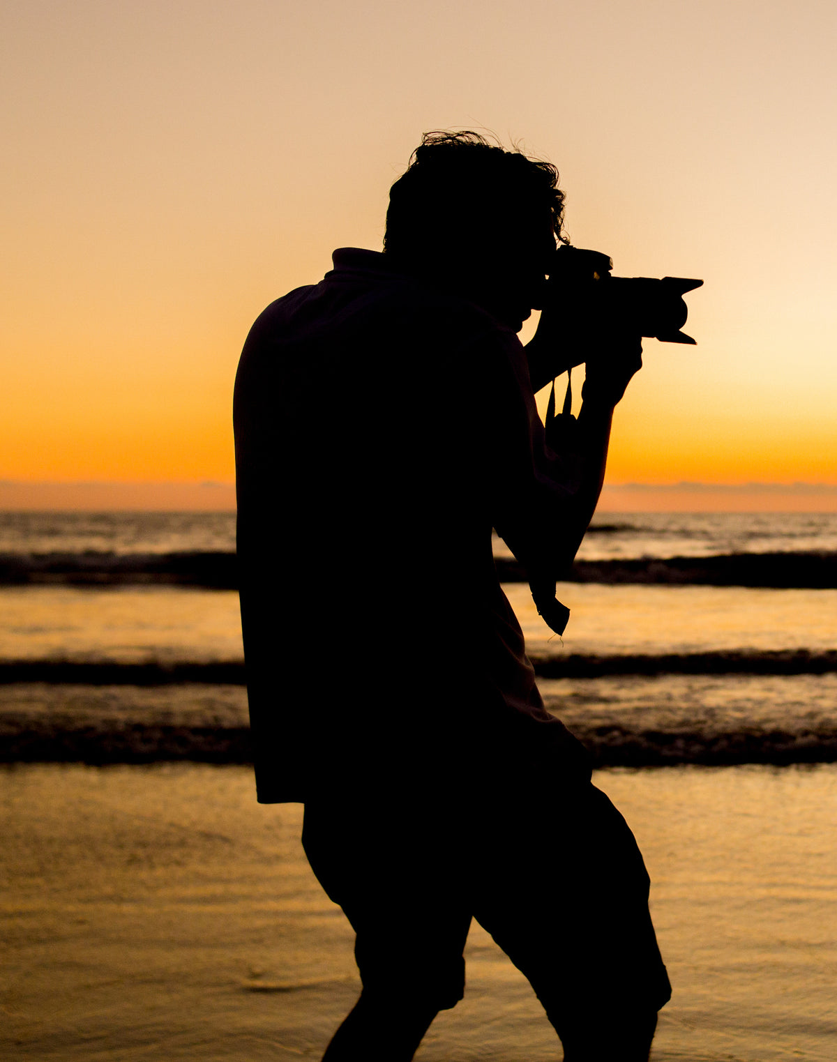Silhouette of a photographer at the shoreline taking pictures against a golden sunset