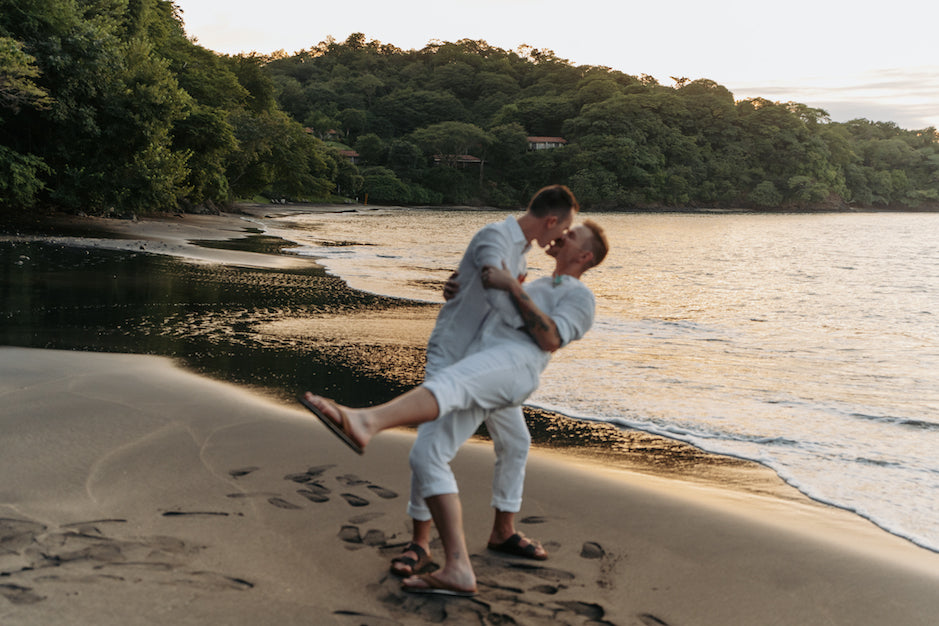 Two grooms in white embrace and dance on the beach at sunset in Costa Rica