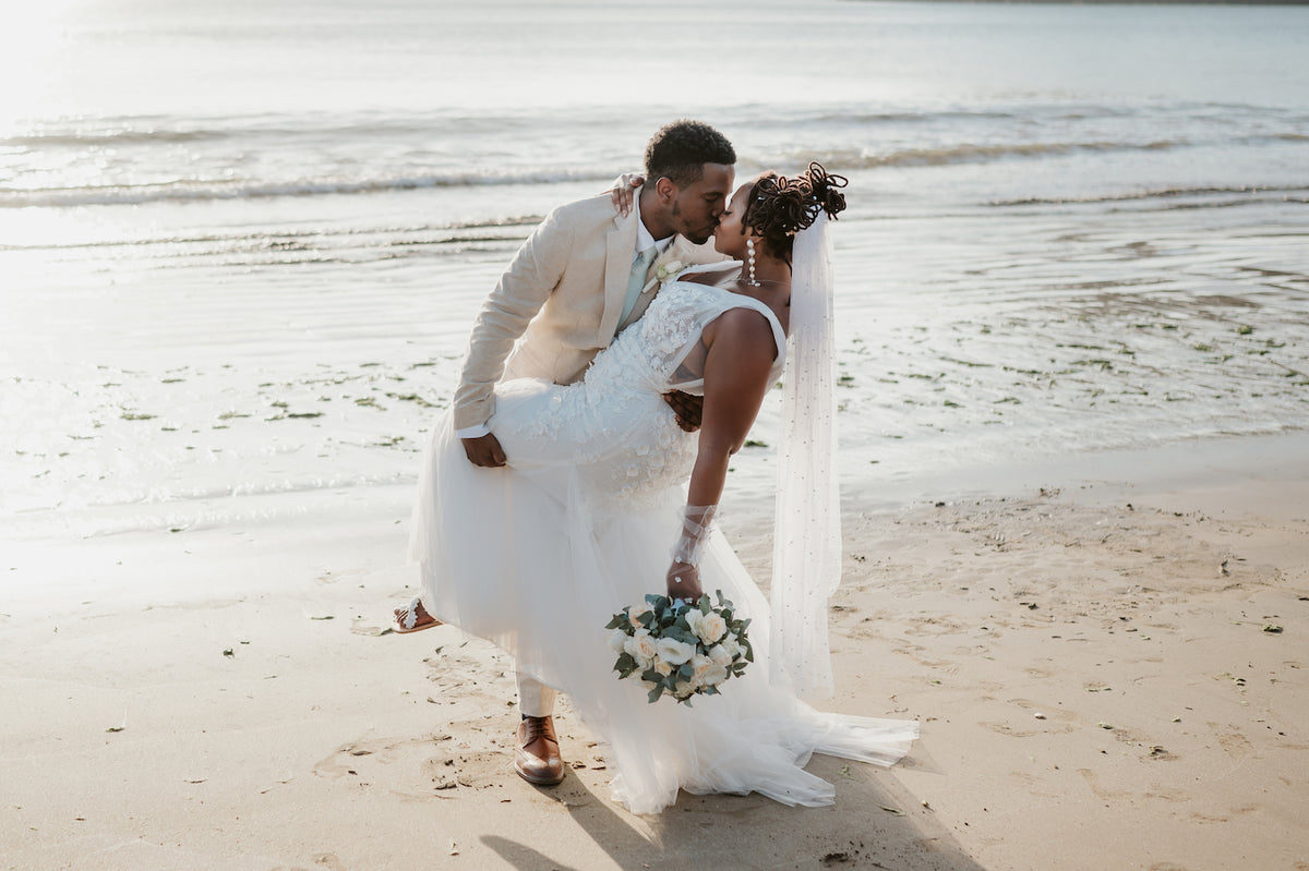 Groom dips and kisses his bride holding a white bouquet on the beach at a Costa Rica wedding