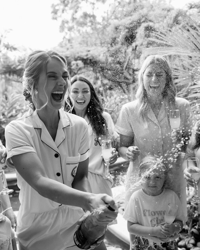 Bride sprays champagne with her bridesmaids in matching pajamas while getting ready for a Costa Rica wedding
