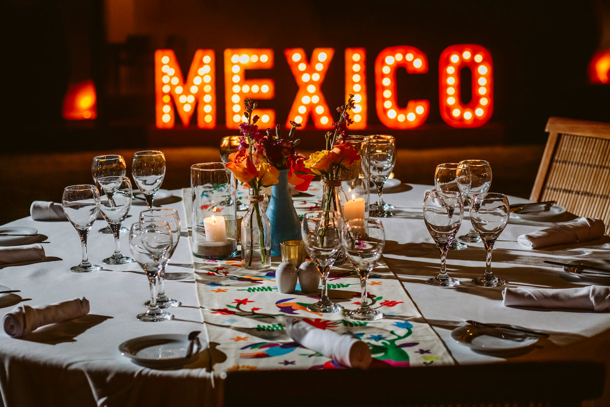 Event table set with colorful Mexican embroidered runner, flowers and candles under a lit-up MEXICO sign