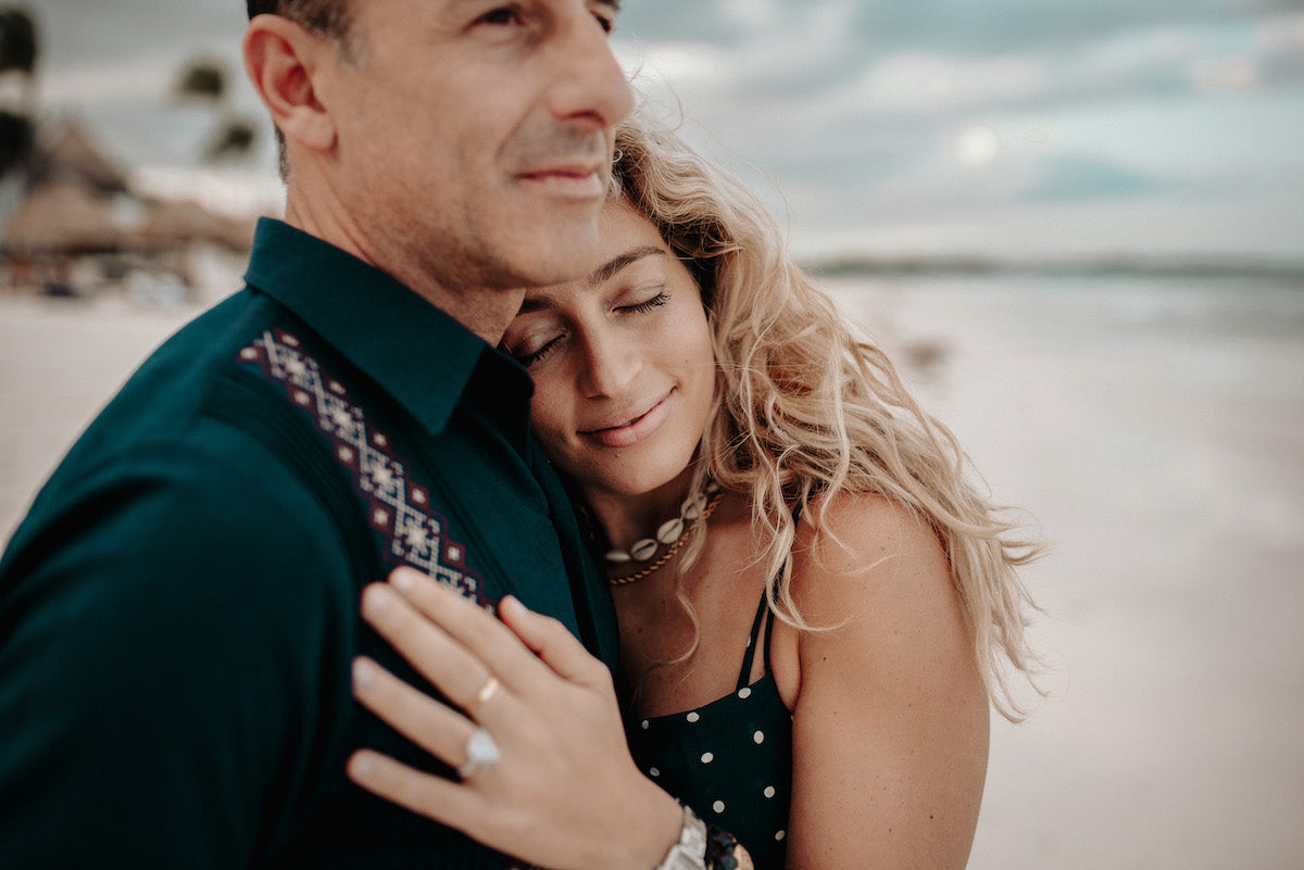 Woman rests her head on her partner's chest during a couples photoshoot on the beach at Fairmont Mayakoba