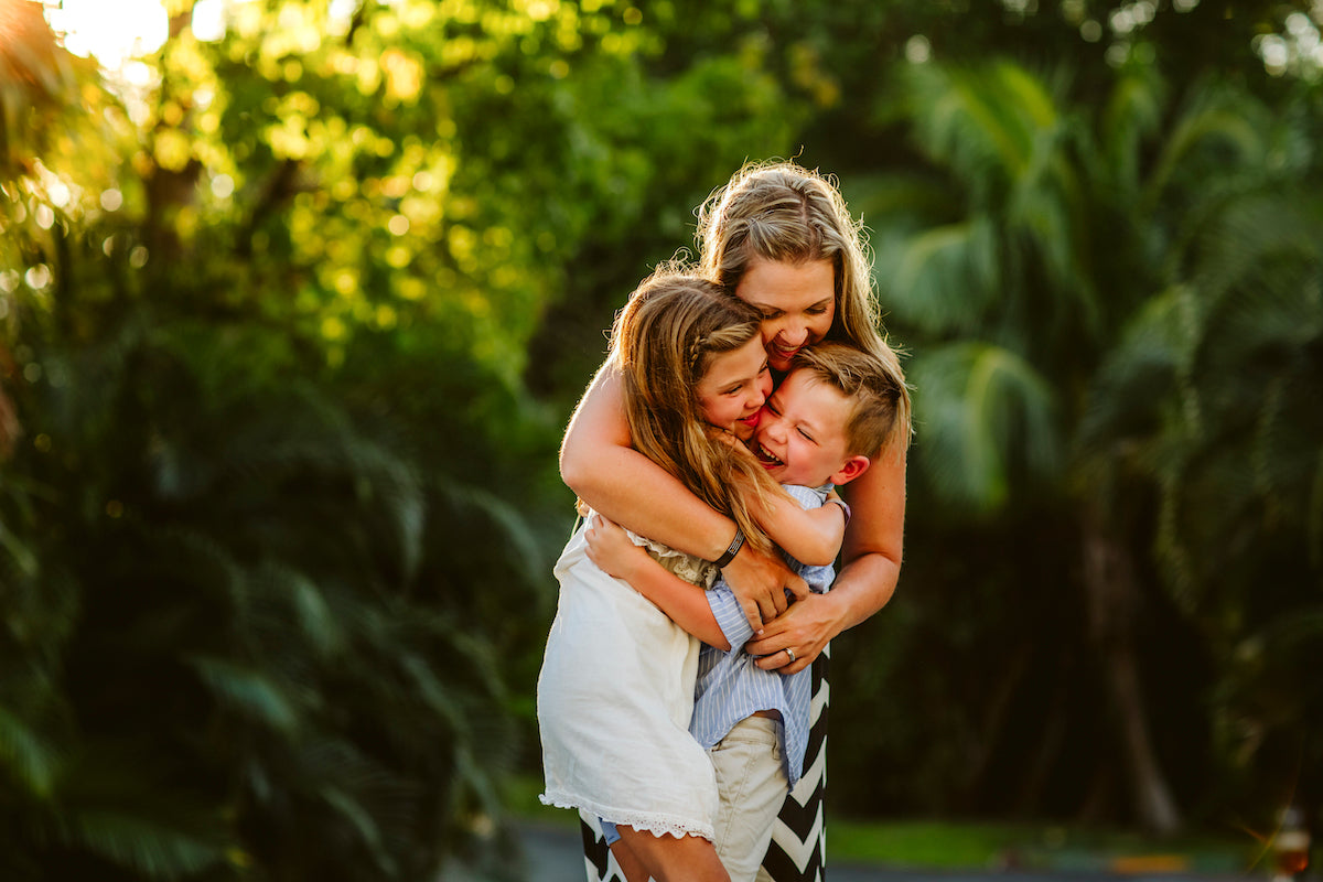 Mother hugs her laughing son and daughter in sunlit tropical gardens at Fairmont Mayakoba