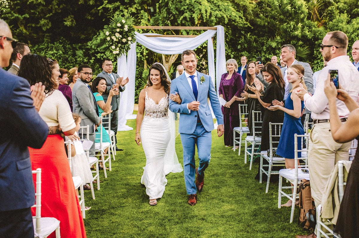 Newlyweds walk back down the aisle as guests applaud at a garden wedding at Fairmont Mayakoba