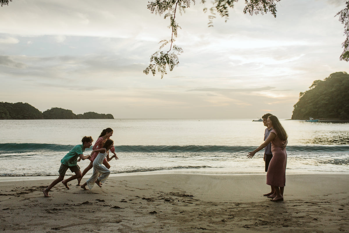 Kids race across the sand as a woman watches during a sunset family photoshoot in Guanacaste, Costa Rica