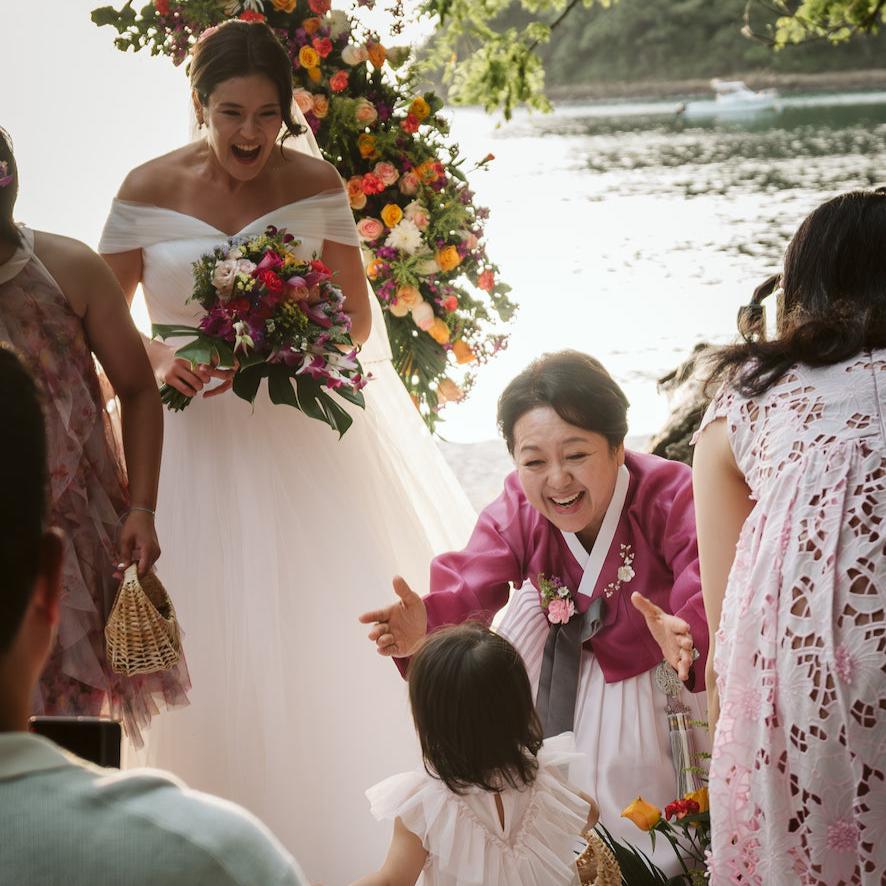 Laughing bride with a colorful bouquet as a guest in a hanbok greets a little girl at a Guanacaste wedding