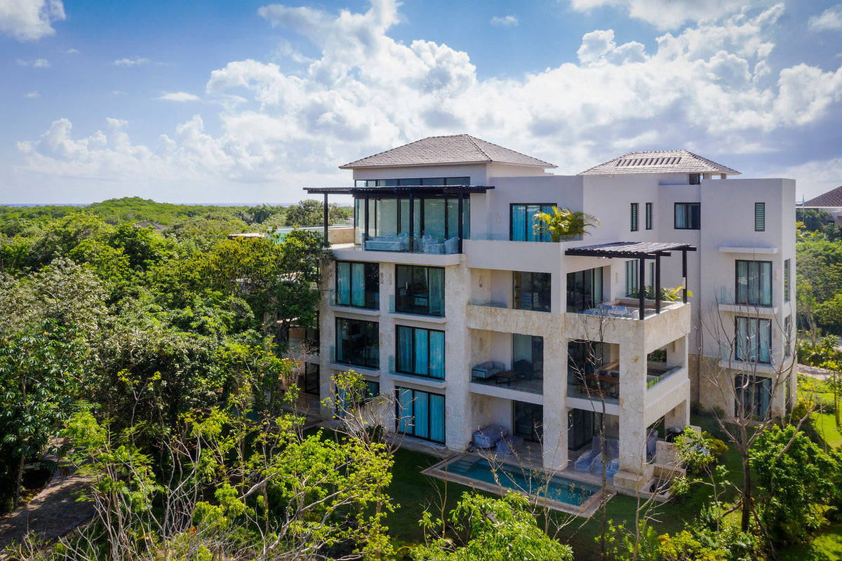Drone view of a modern white residence building with a pool surrounded by tropical jungle