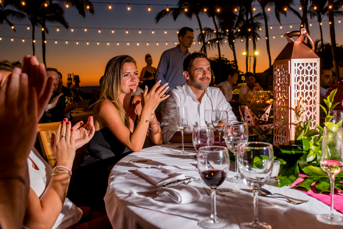 Wedding guests clapping at a candlelit dinner table under string lights at dusk