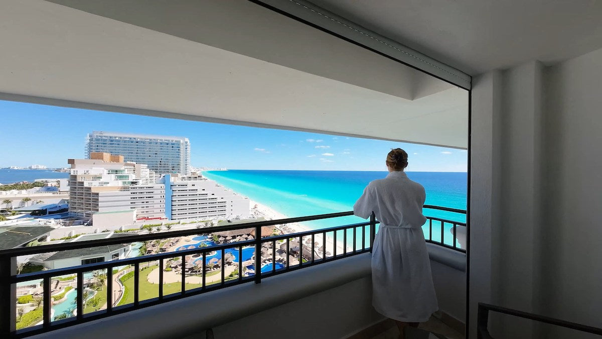 Person in a white robe on a balcony overlooking the beach and turquoise sea at JW Marriott Cancun
