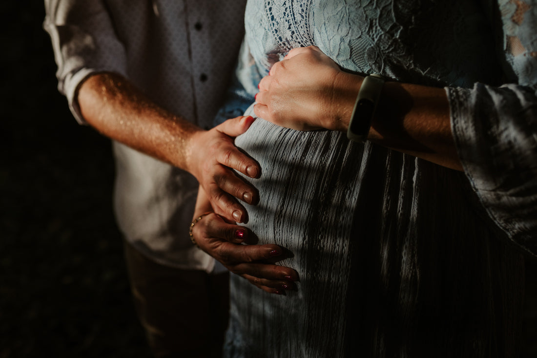 Couple's hands rest together on a baby bump in dramatic low light during an intimate maternity photoshoot