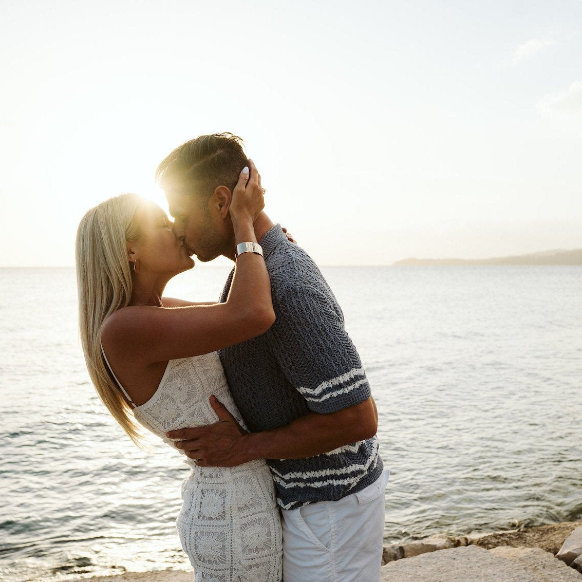 Couple kisses on the rocky shore with the sun flaring behind them in Montego Bay