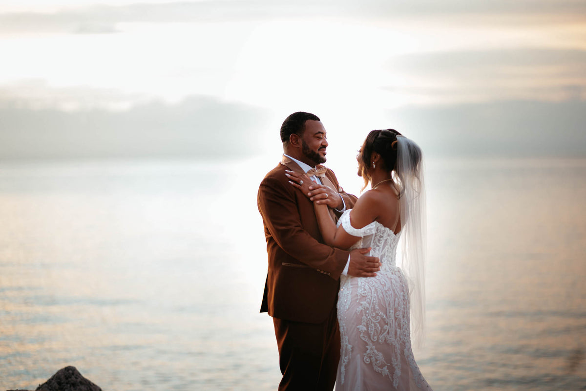 Bride and groom embrace by the sea at sunset during a wedding photoshoot in Montego Bay