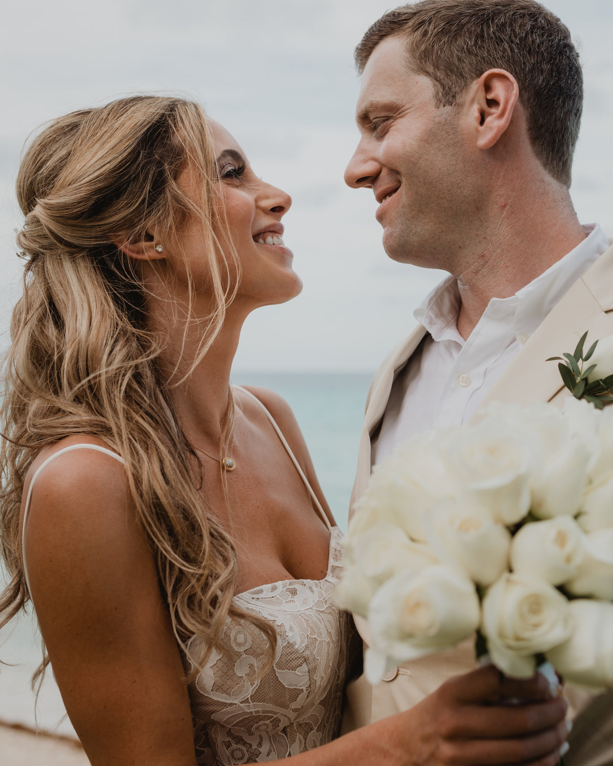 Close-up of a smiling bride and groom gazing at each other with a white rose bouquet in Cancun