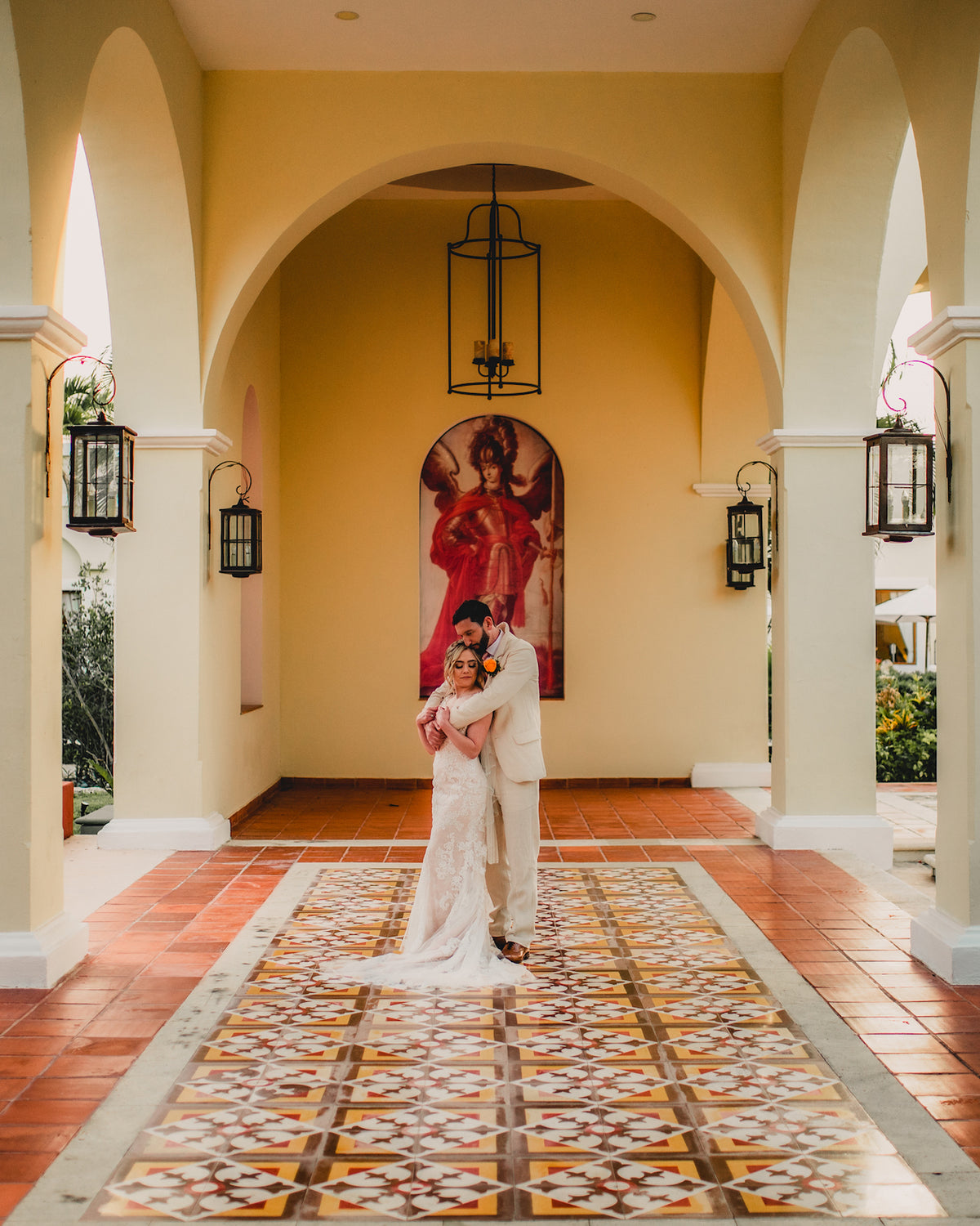 Bride and groom embrace under the arches of a colonial-style hall with patterned tiles in Mexico
