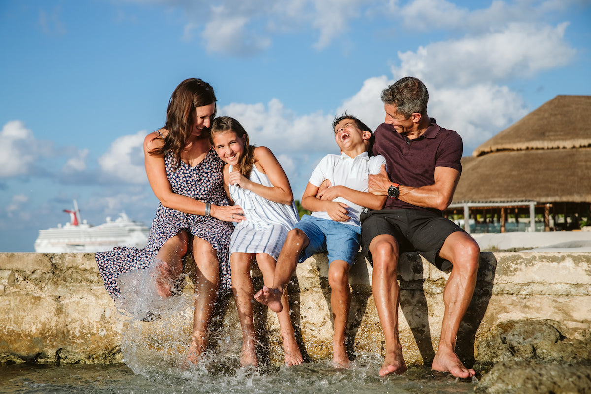 Family of four laughs and splashes their feet in the sea from a stone ledge at InterContinental Presidente Cozumel