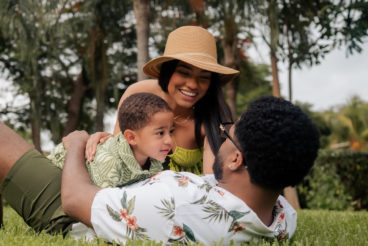 Smiling family with a young boy relaxing on the lawn under palm trees during a family photoshoot
