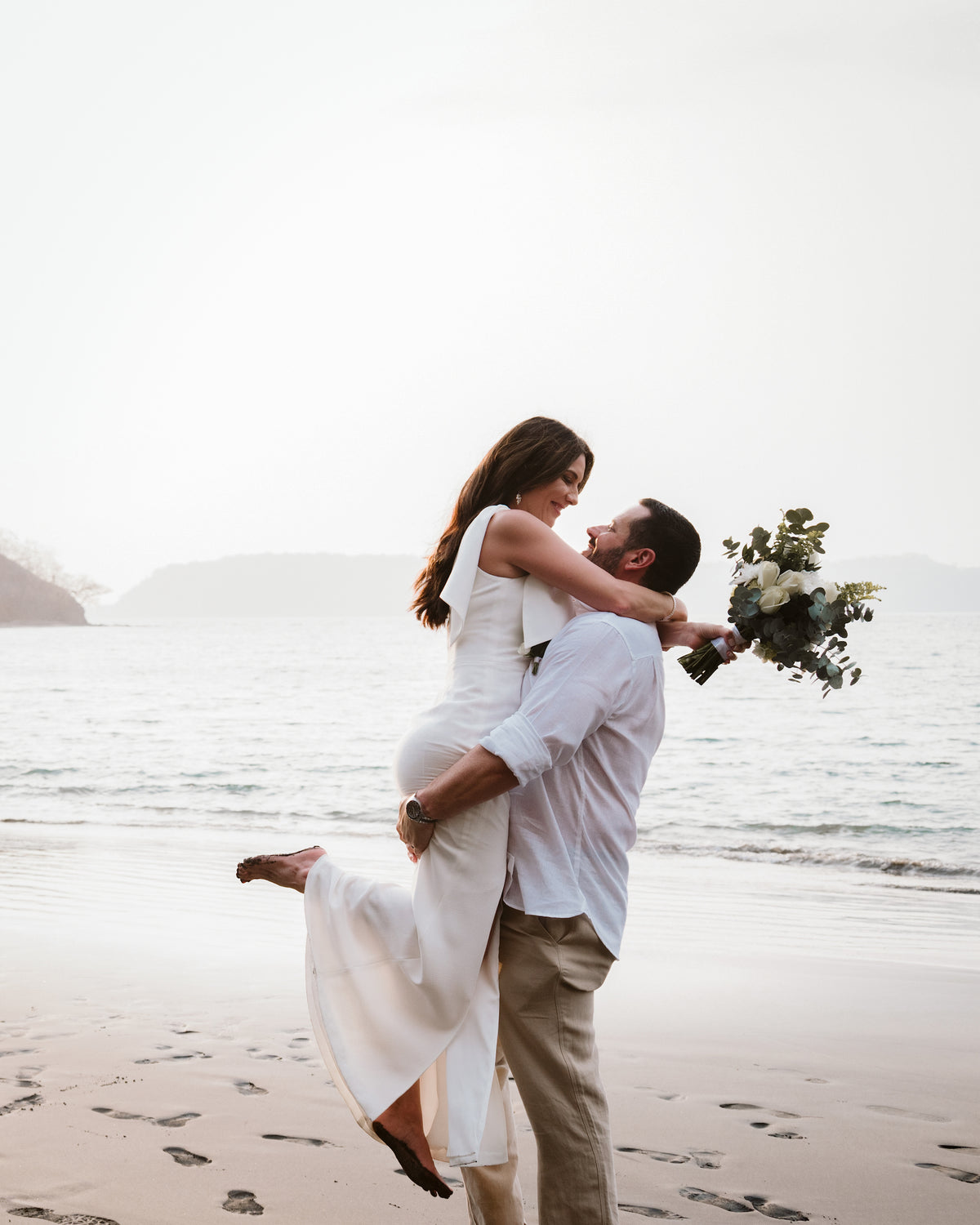 Groom lifts his bride with her bouquet held high on the beach at Secrets Papagayo Costa Rica